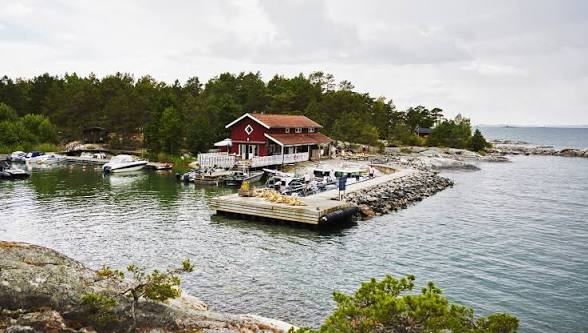 The red Grundet restaurant with its white railings by a small harbour with moored motorboats and a stone breakwater on Rögrund, reached by boat in the Stockholm archipelago