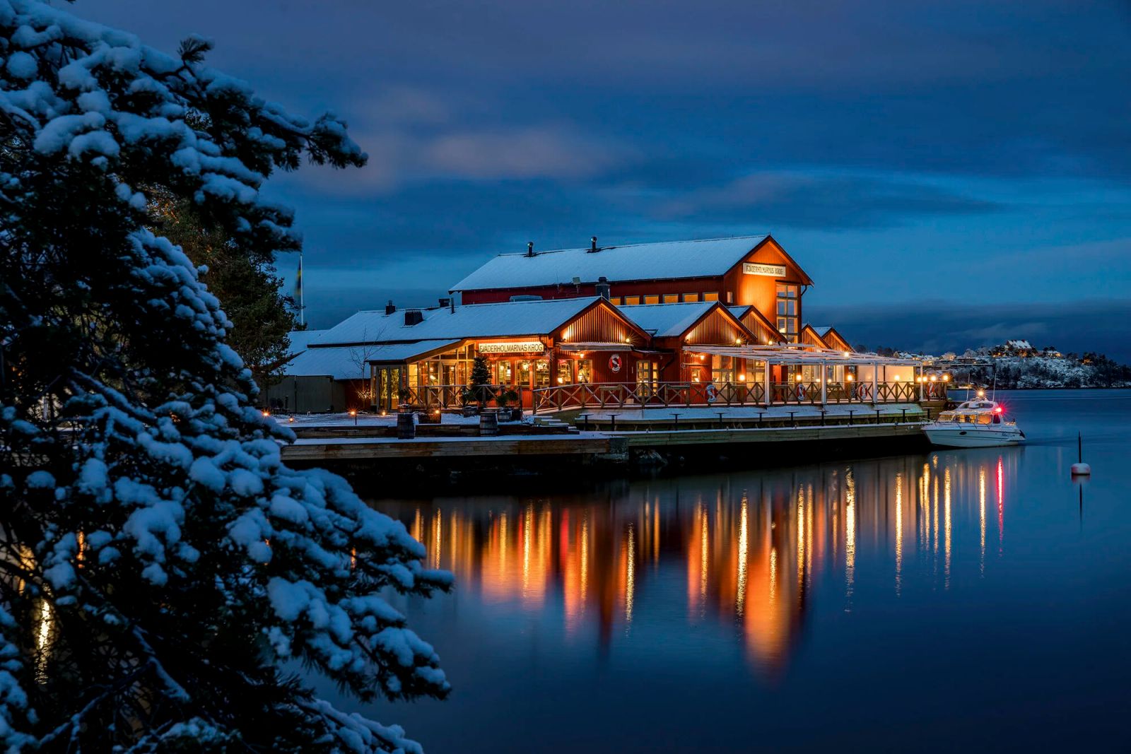 Snow-covered waterfront restaurant with warm lit windows on a winter evening in the Stockholm archipelago