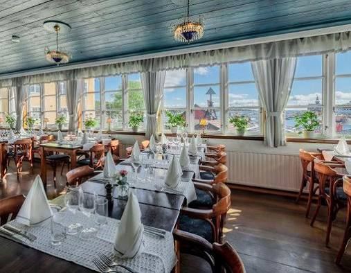 Dining room with white tablecloths, chandeliers and large windows looking out over the water at Sandhamns Värdshus in the Stockholm archipelago