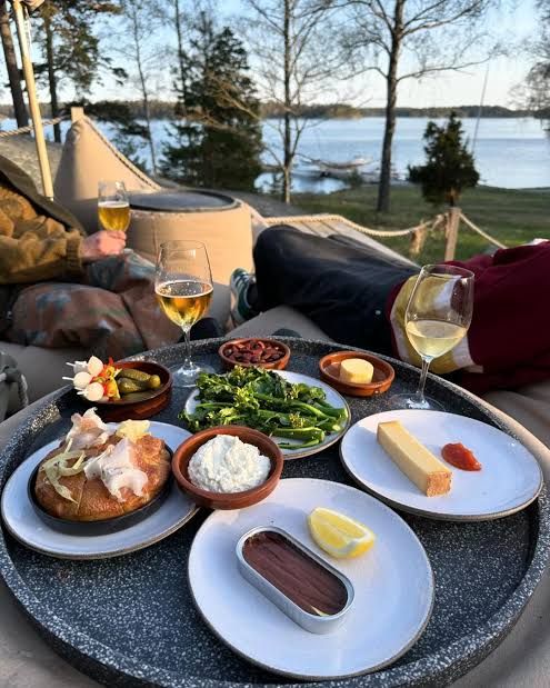 Small plates, bread and glasses of white wine on a tray with a view over the water and wooded shore at Svartsö Krog, Stockholm archipelago