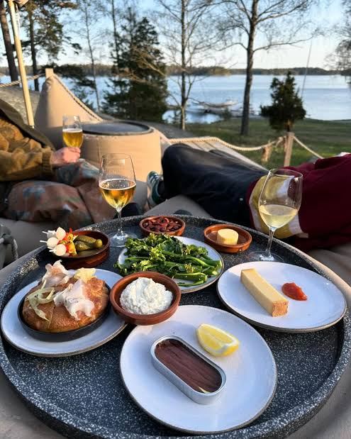 Small plates, bread and glasses of white wine on a tray with a view over the water and wooded shore at Svartsö Krog, Stockholm archipelago