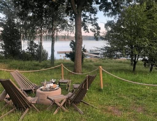 Wooden deck chairs around a fire pit on the lawn above the water and jetties at Svartsö Krog in the Stockholm archipelago