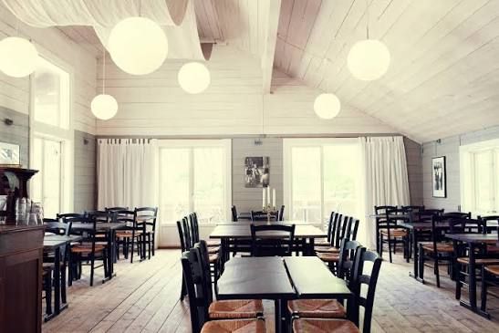 Bright dining room with white wooden walls, globe lamps and dark wooden tables at Svartsö Krog in the Stockholm archipelago