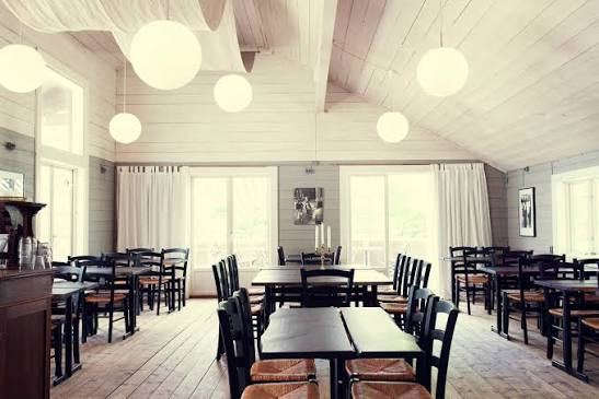 Bright dining room with white wooden walls, globe lamps and dark wooden tables at Svartsö Krog in the Stockholm archipelago