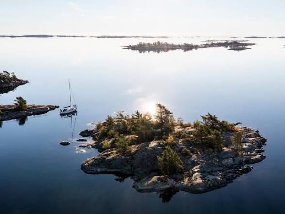 Rocky islet and an anchored sailing boat on calm water off Ornö in the Stockholm archipelago