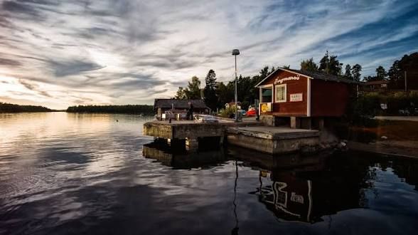 Red boathouse and jetty reflected in still water under an evening sky on Ingmarsö, Stockholm archipelago