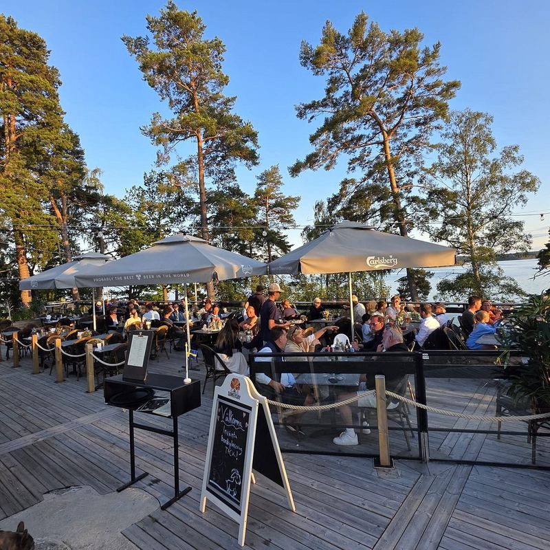 Guests on the outdoor deck under parasols and pine trees at Getfoten