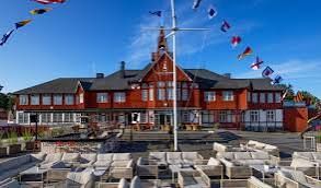 White lounge sofas on a deck in front of the red, towered Seglarhotellet building with flags and bunting on Sandhamn, Stockholm archipelago