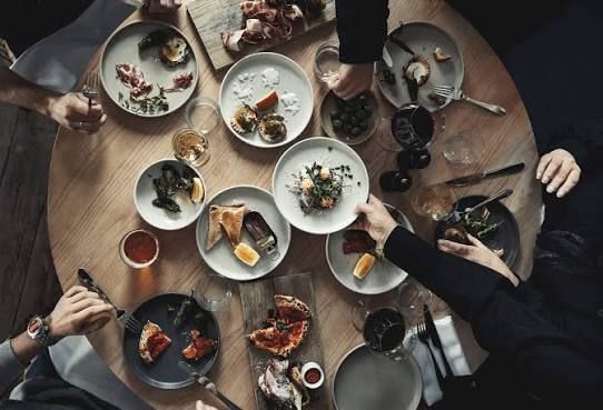 Overhead view of shared small plates, bread and wine on a round wooden table at Seglarhotellet on Sandhamn, Stockholm archipelago