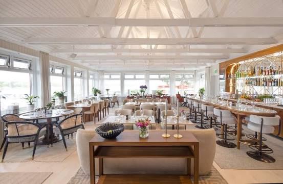 Bright dining room with white beams, large windows and a long bar with stools at Seglarhotellet on Sandhamn, a stop by boat in the Stockholm archipelago