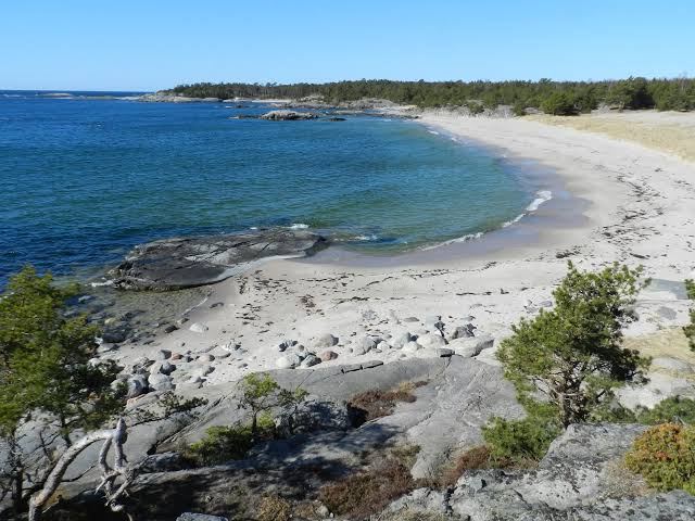 Long sandy beach and smooth granite rocks along a blue bay on Utö