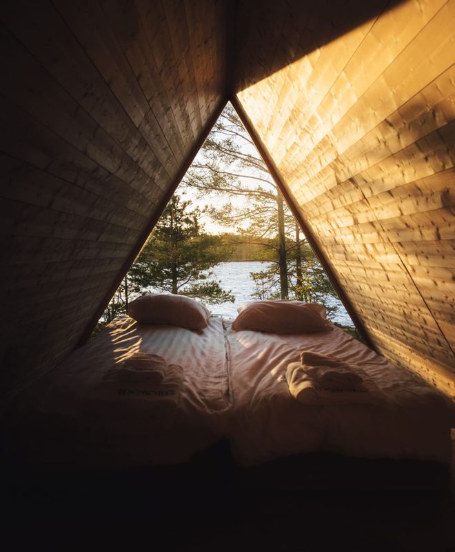 A-frame cabin bedroom with a large window looking out at pine trees and the water on Idöborg