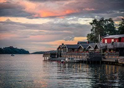 Rökeriet's waterfront buildings and a red house lit up at sunset over calm water on Fjäderholmarna in the Stockholm archipelago