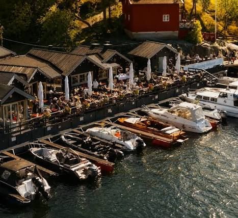 Aerial view of guests on Rökeriet's waterside terrace and boats at its jetty on Fjäderholmarna in the Stockholm archipelago