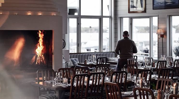 Dining room with an open fire and large windows over the marina at Restaurang J in Nacka Strand, Stockholm