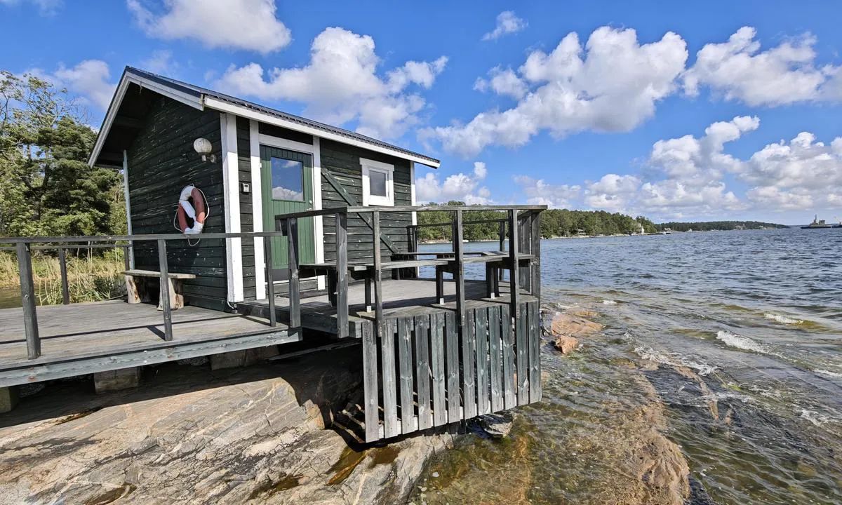 Small grey wooden cabin with a deck on smooth granite rock by the water at Getfoten