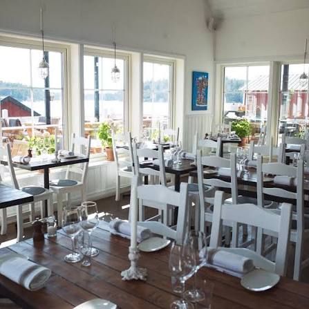 White dining room with set tables and windows over the water and red wooden houses at Ingmarsö Krog in the Stockholm archipelago