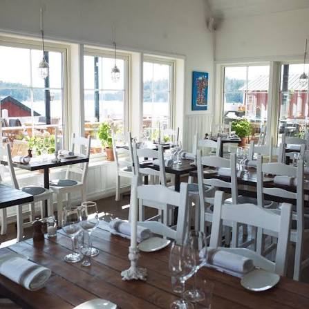 White dining room with set tables and windows over the water and red wooden houses at Ingmarsö Krog in the Stockholm archipelago