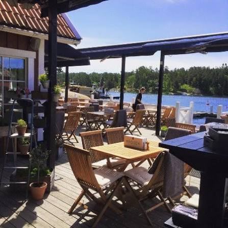 Sunny covered deck with wooden tables and chairs looking out over the water at Ingmarsö Krog, a waterside stop by boat in the Stockholm archipelago