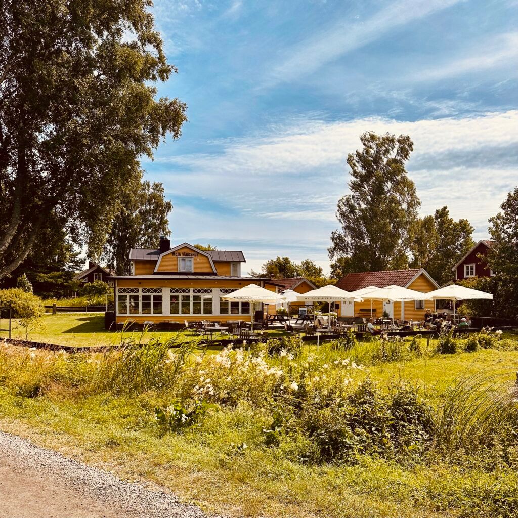 Yellow wooden house with outdoor dining under white parasols on Möja