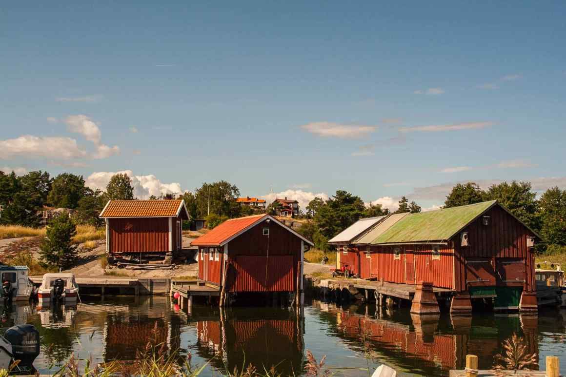 Red wooden boathouses reflected in the water on Möja
