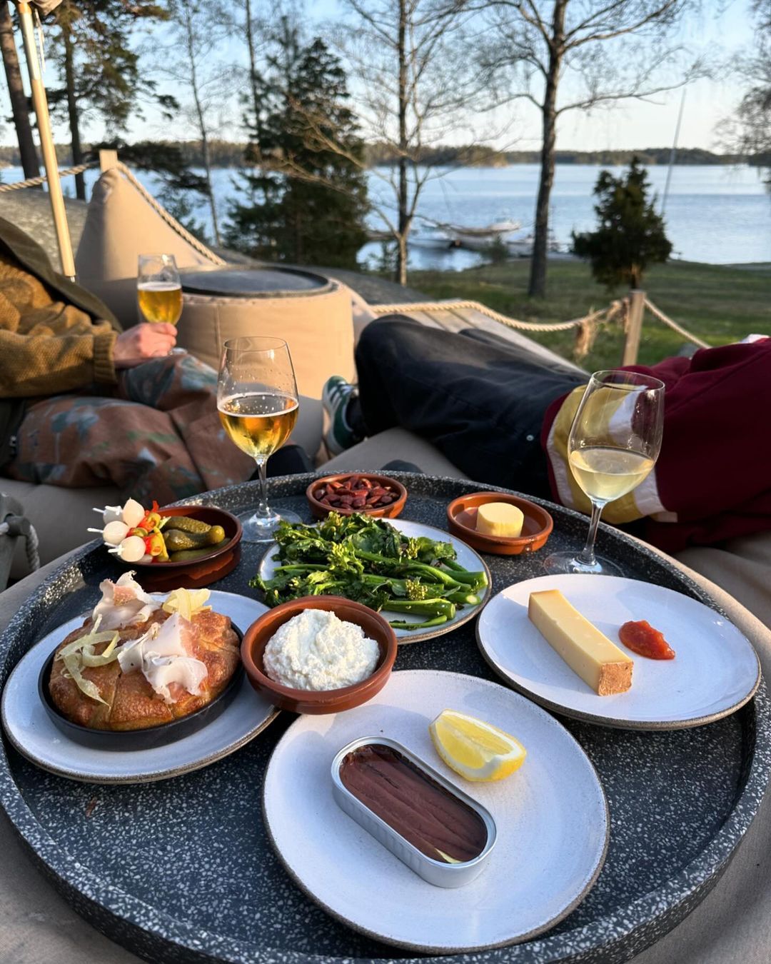 Shared plates of food and glasses of white wine on a table by the water on Svartsö