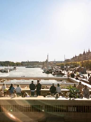 Guests on an upper deck at Strandbryggan looking out over moored boats and the waterfront of Strandvägen in Stockholm