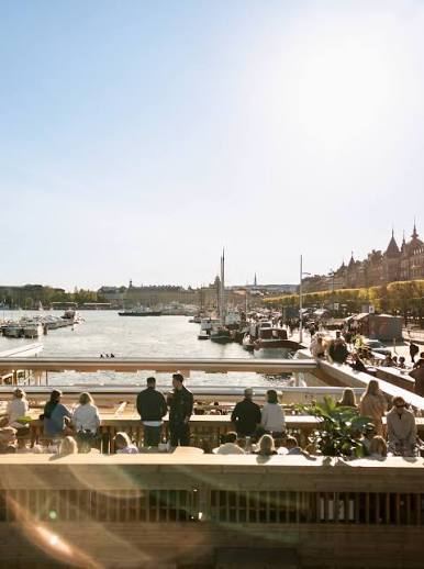 Guests on an upper deck at Strandbryggan looking out over moored boats and the waterfront of Strandvägen in Stockholm