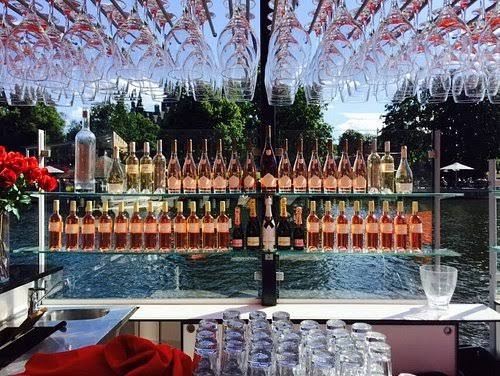 Rows of rosé and sparkling wine bottles beneath hanging wine glasses at the bar at Strandbryggan in Stockholm
