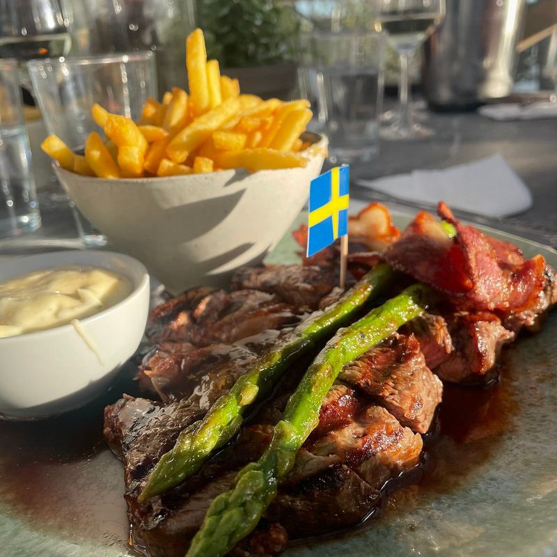 Grilled steak with green asparagus and fries, topped with a small Swedish flag, served at Getfoten