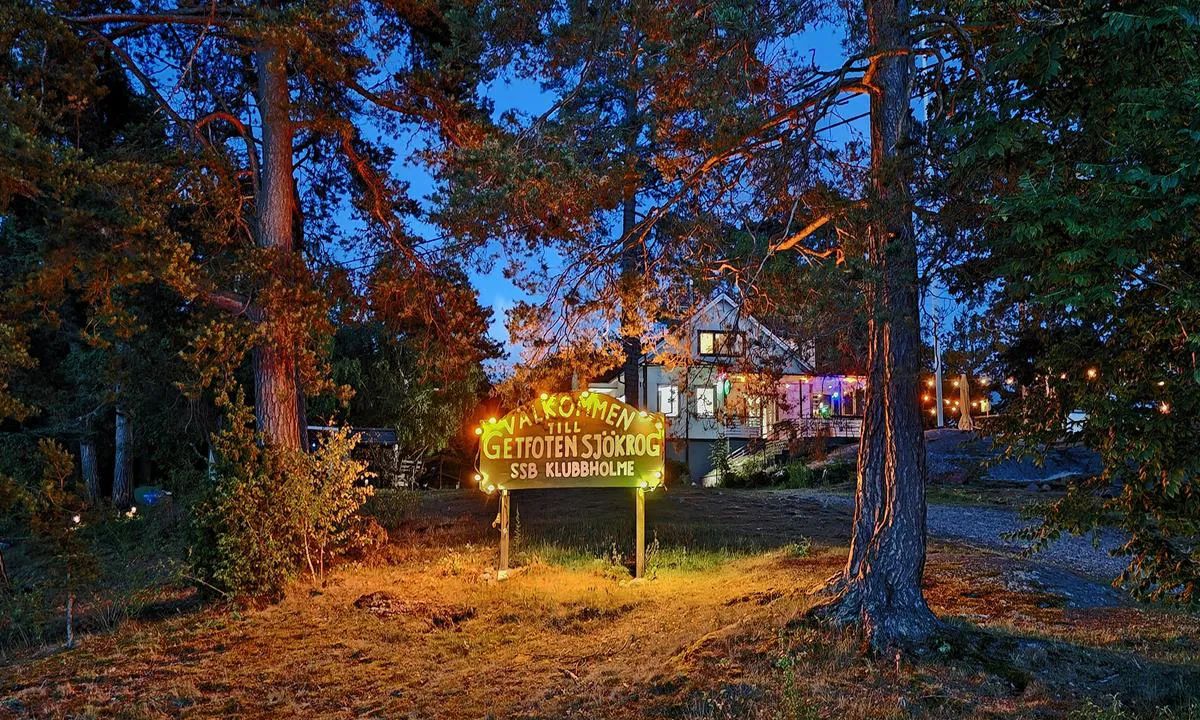 Illuminated Getfoten Sjökrog welcome sign among pine trees at dusk