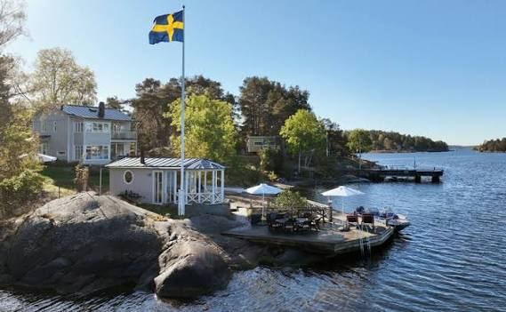 Swedish flag, white house and waterside terrace by a jetty near Harö in the Stockholm archipelago