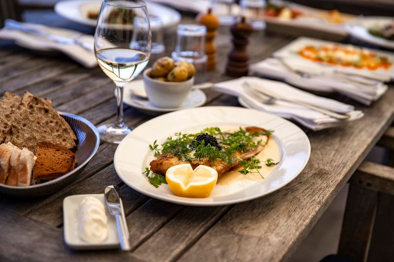 Fish dish with lemon, bread and a glass of white wine on an outdoor table on Grinda