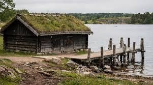 Wooden boathouse with a turf roof and a small jetty on the shore at Birka