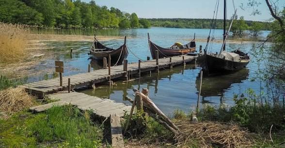 Replica Viking boats moored at a wooden jetty in a reed-lined bay at Birka