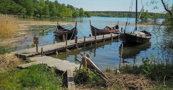 Replica Viking boats moored at a wooden jetty in a reed-lined bay at Birka
