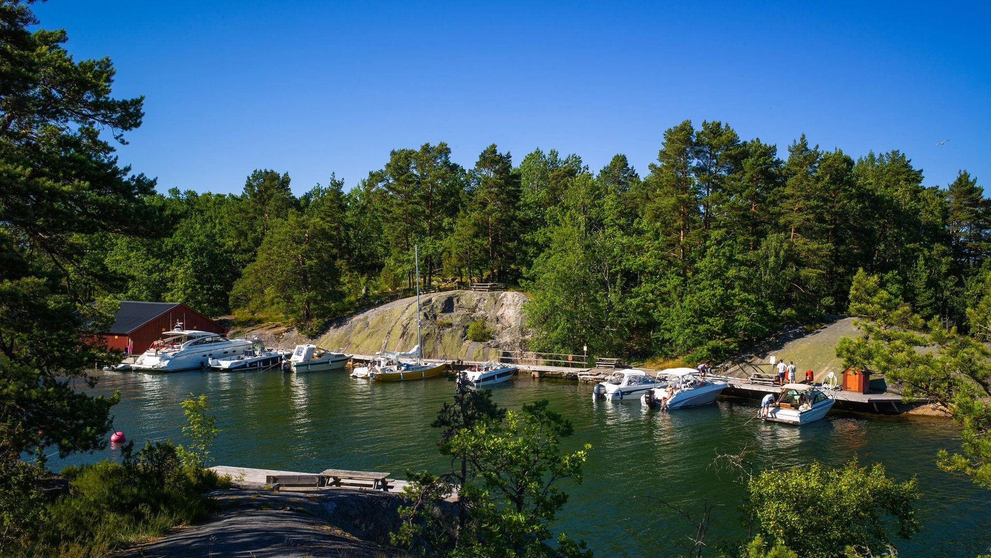 Pine-covered granite cliffs and boats at a jetty in a calm Finnhamn bay