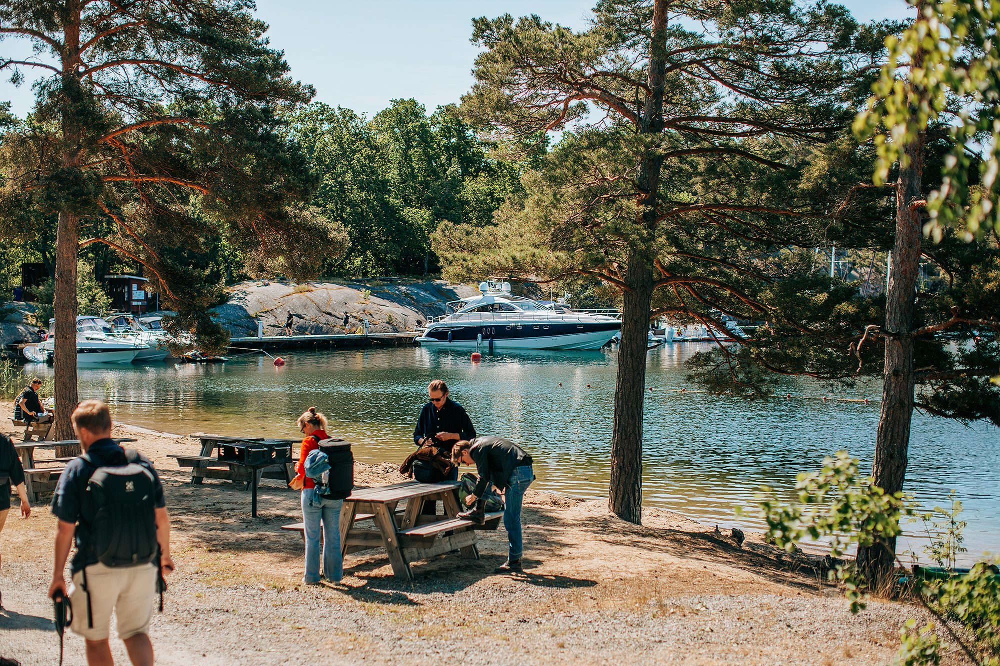 Picnic table under a pine tree by a Finnhamn bay, with a motorboat at anchor