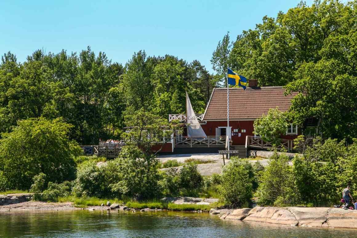Finnhamn waterfront in summer – a red wooden building, Swedish flag and granite shoreline