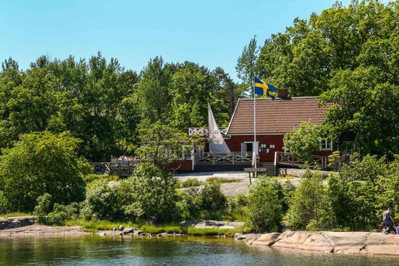Finnhamn waterfront in summer – a red wooden building, Swedish flag and granite shoreline