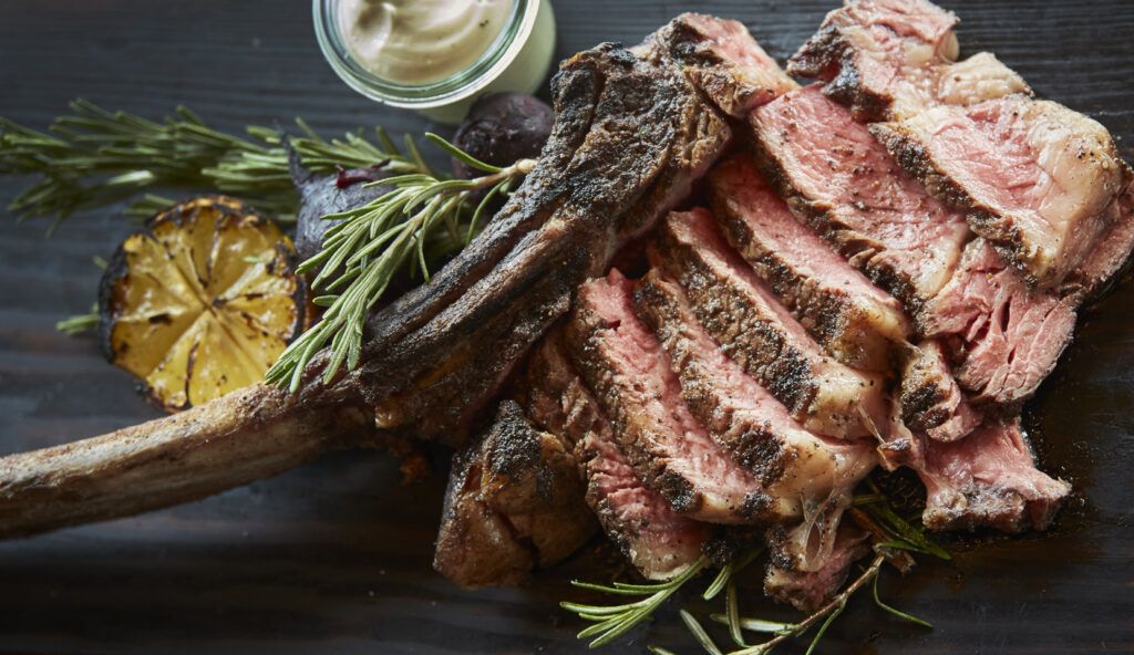 Sliced grilled tomahawk steak with rosemary and charred lemon at The Old Smokehouse
