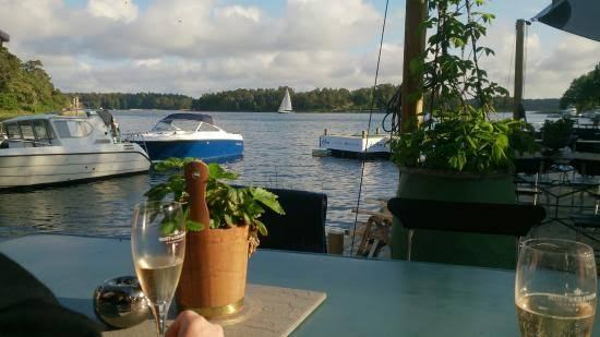 Glasses of sparkling wine on a waterside table, with motorboats and a sailboat on the bay, at Motorverkstan Bistro & Bar on Djurö, Stockholm archipelago