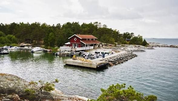 The red Grundet restaurant with its white railings by a small harbour with moored motorboats and a stone breakwater on Rögrund, reached by boat in the Stockholm archipelago