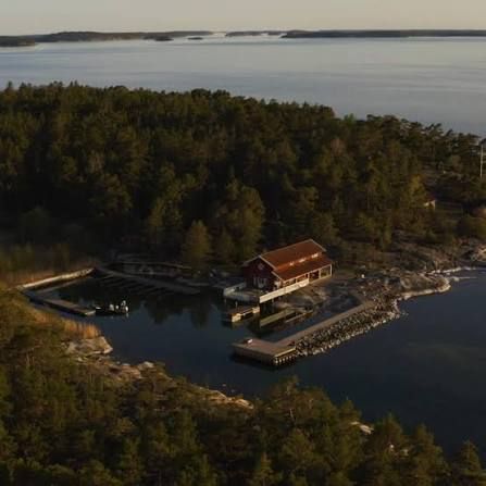 Grundet's red restaurant and its small harbour from the air, with forested Rögrund and open water beyond, in the Stockholm archipelago