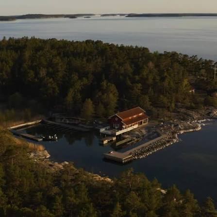 Grundet's red restaurant and its small harbour from the air, with forested Rögrund and open water beyond, in the Stockholm archipelago