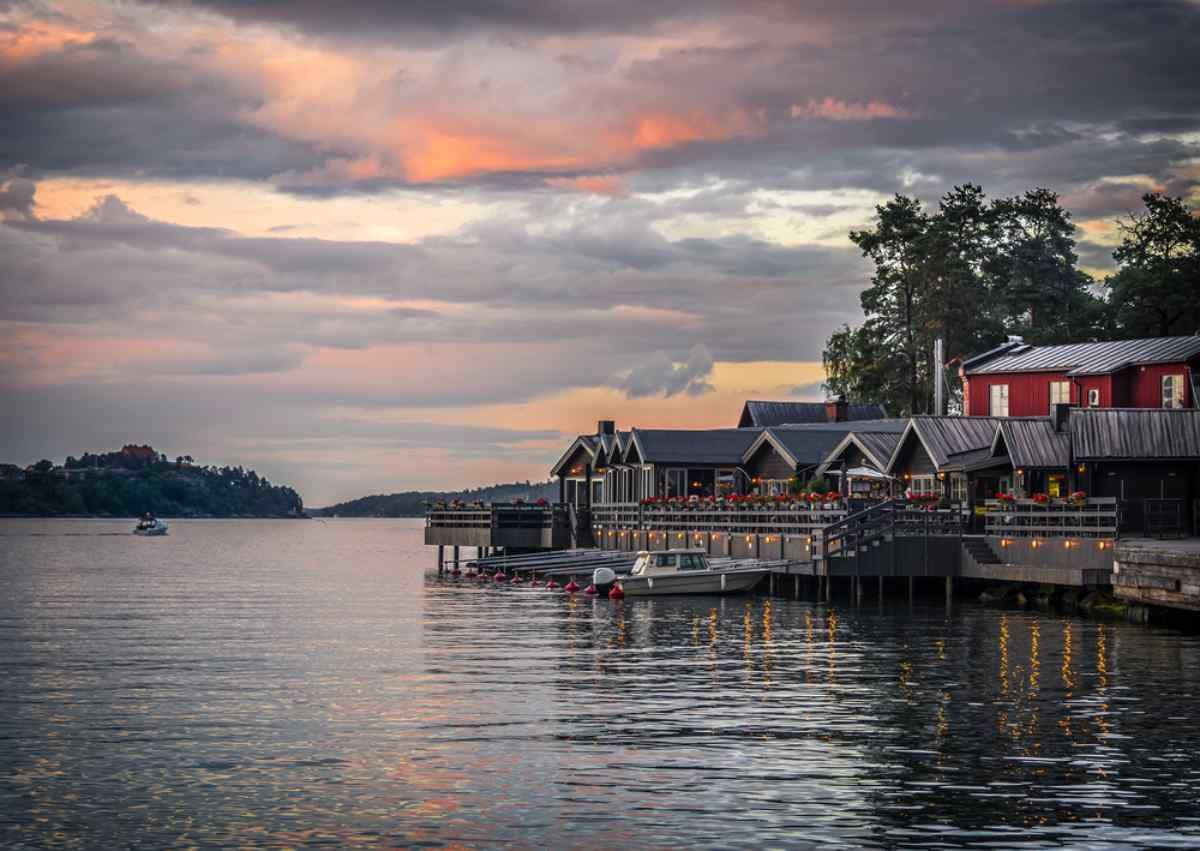 Waterfront restaurant buildings on Fjäderholmarna under a dramatic sunset sky
