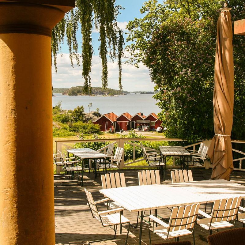 Outdoor terrace tables between yellow columns at Grinda Wärdshus, overlooking the bay