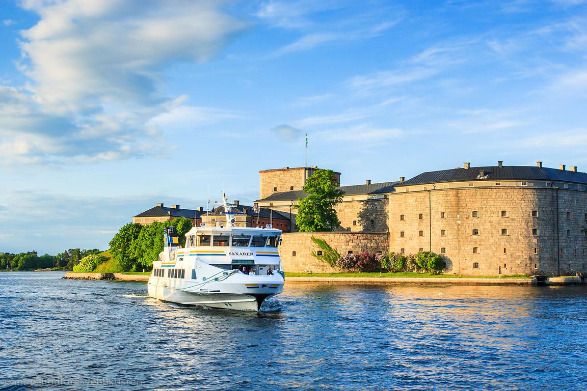 A white passenger boat passing the stone walls of Vaxholm Fortress