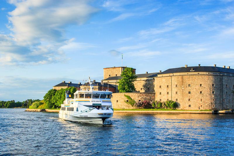 A white passenger boat passing the stone walls of Vaxholm Fortress