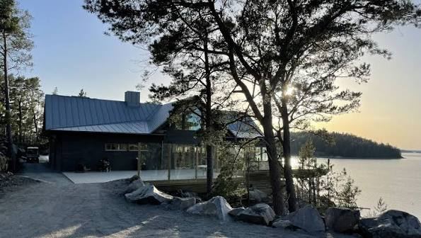 Dark wooden building among pine trees on the Idöborg shoreline at sunset